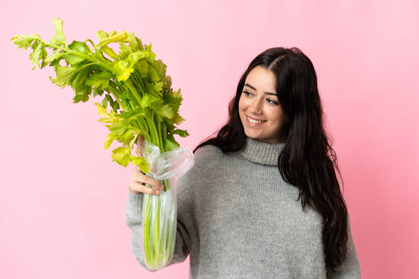 Young caucasian woman holding a celery isolated on blue background with happy expression - Photo, Image
