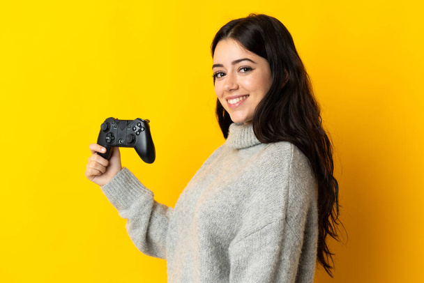 Woman playing with a video game controllerisolrted on yellow background smiling a lot - 写真・画像