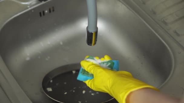 Χέρια σε κίτρινα προστατευτικά γάντια απλώστε απορρυπαντικό και πλύνετε το τηγάνι  - Πλάνα, βίντεο