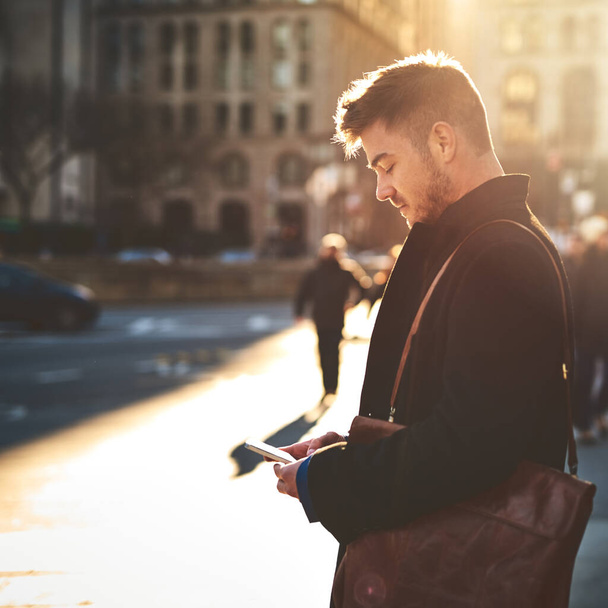 On my way to the office. Shot of a focused young man texting on his phone while standing in the busy streets of the city on his way to work. - Valokuva, kuva