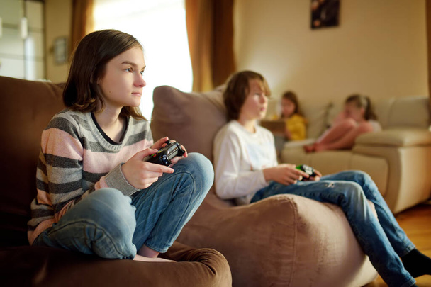 A group of preteen kids playing video games at home. Children sitting on the couch together holding gaming controllers. Family leisure and fun indoors. - Photo, image
