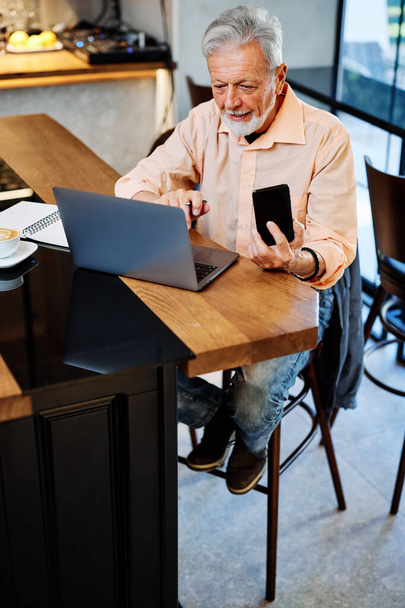 Un étudiant âgé contemporain souriant assis dans un café et ayant un appel vidéo en pause. Étudiant senior au café. - Photo, image