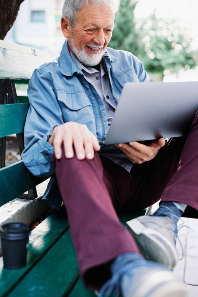 Šťastný starší student sedí na lavičce v parku a drží notebook v klíně. Senioři v rekvalifikaci. - Fotografie, Obrázek