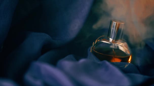 Bottle of perfume on blue fabric in cloud of smoke. Close-up slow motion video. - Footage, Video