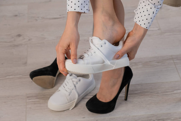 Close-up business woman takes off her shoes puts on white leather sneakers. - Foto, immagini