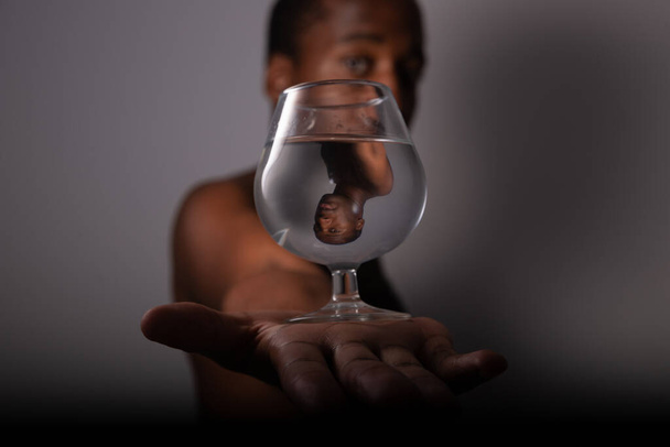 Um rapaz segura um copo de água numa mão e olha para o seu reflexo. Concentre-se na reflexão no vidro de água e fundo fora de foco - Foto, Imagem