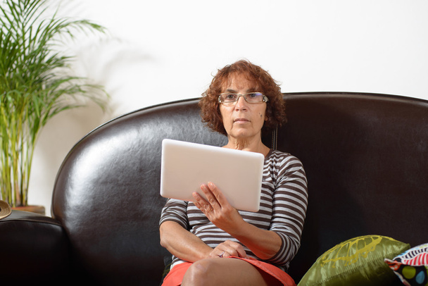 una mujer mayor en un sofá con una tableta digital
 - Foto, Imagen