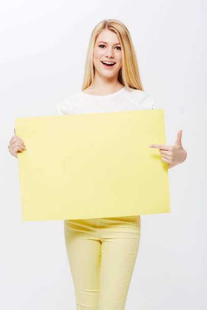 Put your copyspace right here. A pretty young blonde woman holding a blank placard up for your copyspace. - Photo, Image
