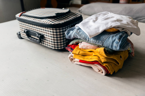 Csomó holmi, színes ruhák és bőröndök az ágyon. Készen áll a csomagolásra egy nyaralás nyaralás. - Fotó, kép