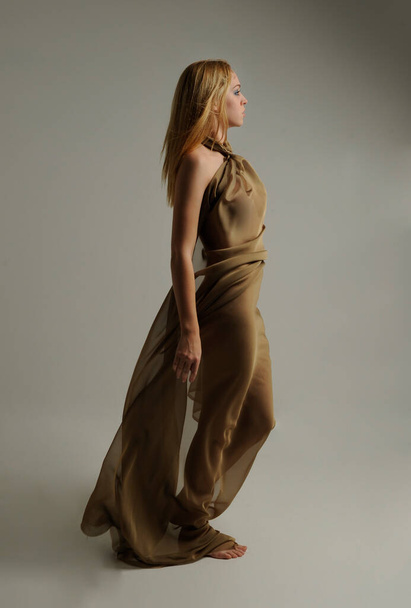  Full length portret van mooie vrouwelijke model dragen Griekse godin toga jurk, poseren met elegante gebaar bewegingen op een studio achtergrond. - Foto, afbeelding