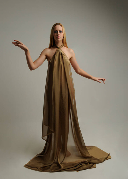  Full length portrait of pretty female model wearing  grecian goddess  toga gown, posing with elegant gestural movements on a studio background. - Foto, Imagem