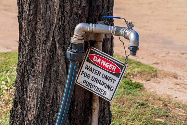 Barajın kıyısındaki ücretsiz bir kamp alanında su içmek için uygun olmadığına dair bir uyarı işareti. Ağaç gövdesine musluk takıldı. - Fotoğraf, Görsel