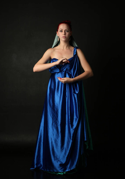  Yunan tanrıçası Toga elbisesi giymiş, stüdyo arka planında zarif hareketlerle poz veren güzel bir kadın modelin tam boy portresi.. - Fotoğraf, Görsel