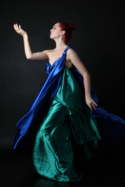  Ganztägiges Porträt eines hübschen weiblichen Modells in einem Toga-Kleid der griechischen Göttin, das mit eleganten gestikulierenden Bewegungen vor Studiohintergrund posiert. - Foto, Bild