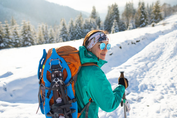 A woman walks with snowshoes on the backpack, winter trekking, a woman in the mountains in winter, hiking equipment - Photo, Image