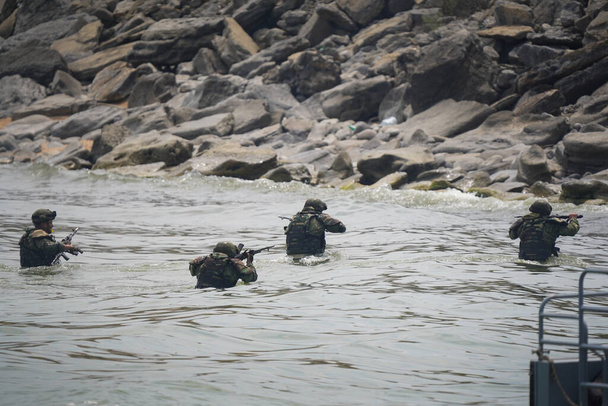 Czterech żołnierzy w mundurach wojskowych wychodzi z wody na brzeg. - Zdjęcie, obraz