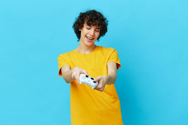 curly guy plays with joystick in yellow t-shirts isolated backgrounds - Фото, зображення