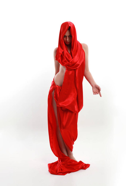Volledig portret van een roodharige vrouw in een mooi sexy zijden jurk, staande houding met creatieve armgebaren, geïsoleerd op witte studioachtergrond. - Foto, afbeelding