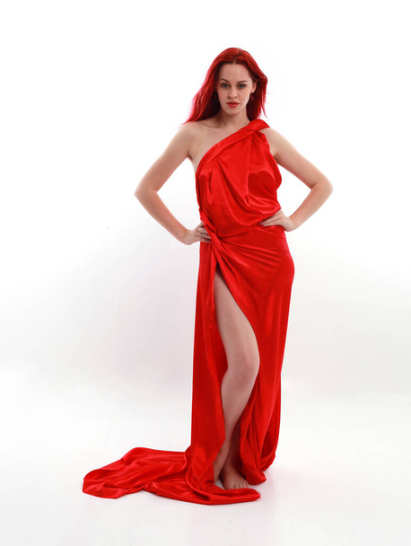 Teljes hosszúságú portré vörös hajú nő visel egy gyönyörű szexi selyem ruha, álló póz kreatív kar gesztusok, elszigetelt fehér stúdió háttér. - Fotó, kép