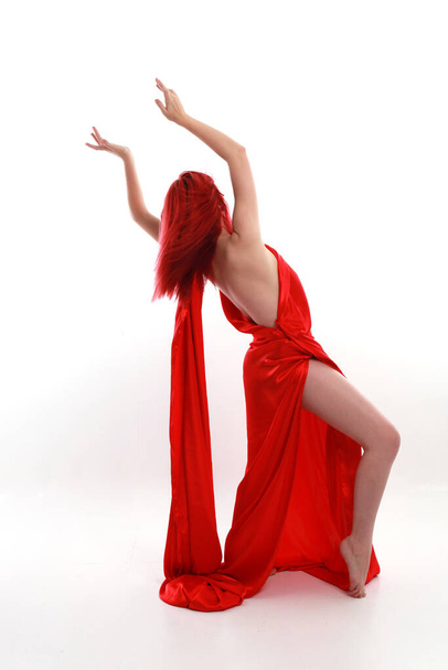 美しいセクシーなシルクのガウンの衣装を身に着けている赤い髪の女性の完全な長さの肖像画,創造的な腕のジェスチャーで立ちポーズ,白いスタジオの背景に孤立. - 写真・画像