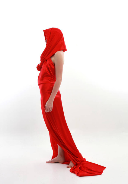 Kızıl saçlı, güzel, ipek bir elbise giyen, yaratıcı kol hareketleriyle ayakta duran beyaz stüdyo arka planında izole edilmiş, uzun boylu bir kadın portresi.. - Fotoğraf, Görsel