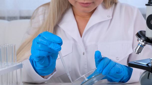 naispuolinen tiedemies laboratorioassistentti käyttää mikropipettejä koeputkien täyttämiseen suuressa nykyaikaisessa laboratoriossa mikroskoopilla tutkittavaksi. - Valokuva, kuva