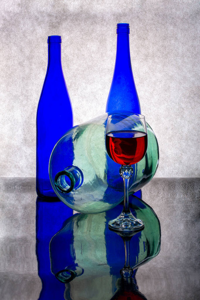 Натюрморт с голубыми бутылками, бокалом красного вина и стеклянной бутылкой - Фото, изображение