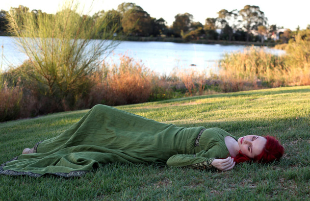 Retrato de cuerpo entero de mujer pelirroja con un hermoso vestido de fantasía medieval verde. Posando con las manos gestuales sobre un fondo de bosque encantado. - Foto, imagen