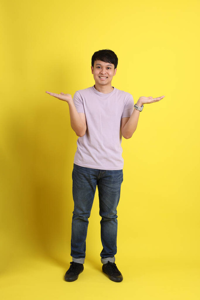 The young adult Asian man standing on the yellow background. - Foto, Imagen