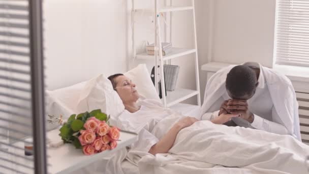 Mediana lentitud de hombre negro molesto vislumbrando a su esposa enferma en el hospital. Mujer con tubo de oxígeno en la nariz durmiendo en la cama del hospital - Metraje, vídeo