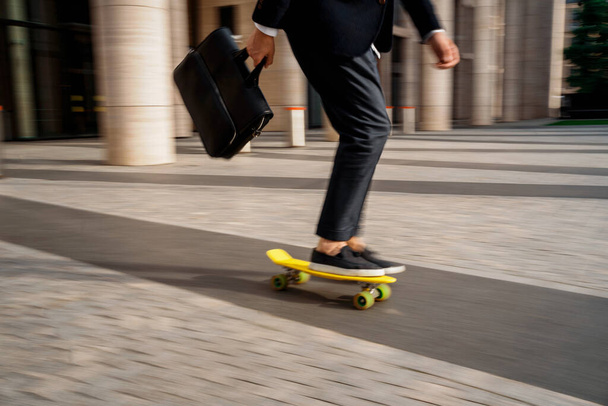 The manager is riding a skateboard in a hurry to a meeting. A male economist rides a board to work with a briefcase. A banker in a business suit. - Zdjęcie, obraz