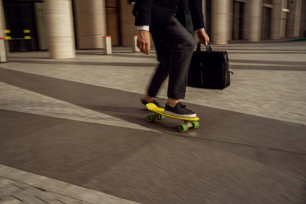 A male entrepreneur is in a hurry to meet. A gray-haired businessman rides a skateboard to work in the office. - Foto, afbeelding
