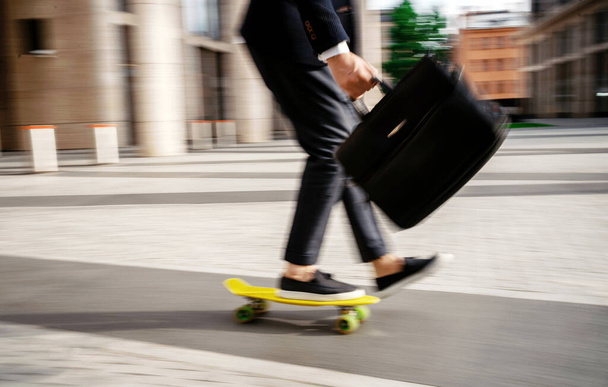 A blurry photo in motion. A businessman manager hurries to a meeting with colleagues, holds a briefcase and rides a skateboard. - Φωτογραφία, εικόνα