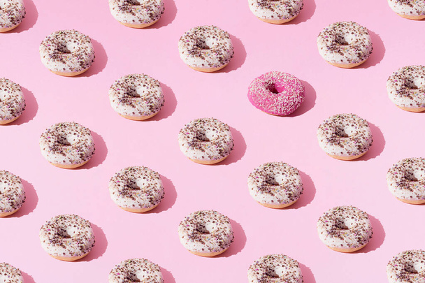 Ring donuts whith white and pink glaze and small colorful crumbs on a pink pastel background. Minimal concept and design. Pattern. Flat lay. - Photo, image