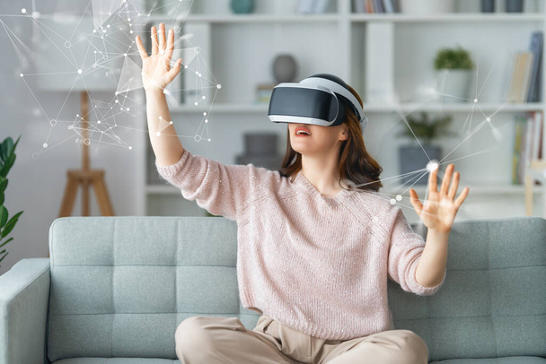 Metaverse technology concept. Woman with VR virtual reality goggles sitting on the sofa at home. Futuristic lifestyle. - Фото, изображение