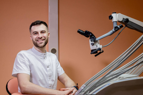 A male dentist looks into a microscope. Modern dentistry using new technologies. - Фото, изображение