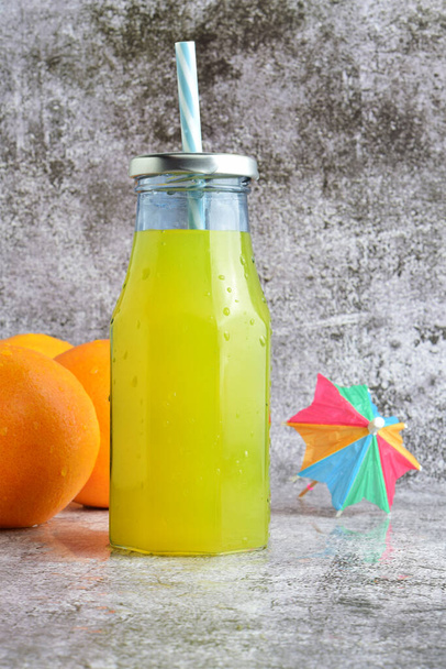 Verticaal schot, glazen fles met verfrissende sinaasappel, stenen voet in lichte kleuren en kopieerruimte. - Foto, afbeelding