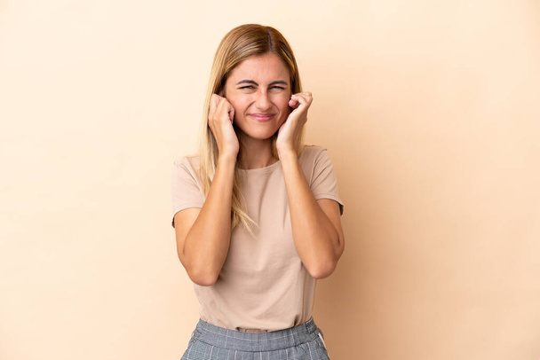 Blonde Uruguayan girl isolated on beige background frustrated and covering ears - Foto, Imagen