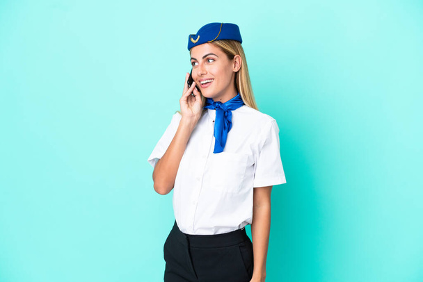Airplane stewardess Uruguayan woman isolated on blue background keeping a conversation with the mobile phone - Foto, afbeelding