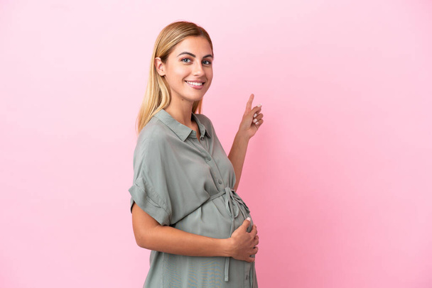 Young Uruguayan woman isolated on blue background pregnant and pointing to the lateral - Photo, Image