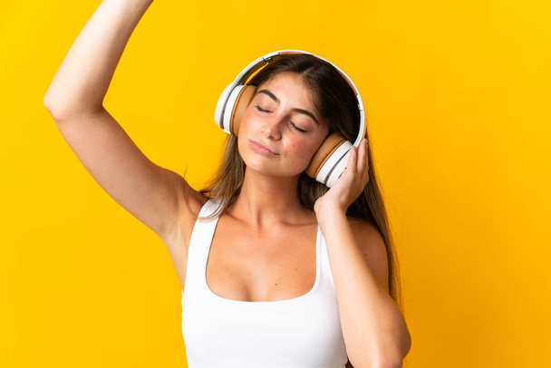 Молодая белая женщина, изолированная на желтом фоне, слушает музыку и танцует - Фото, изображение