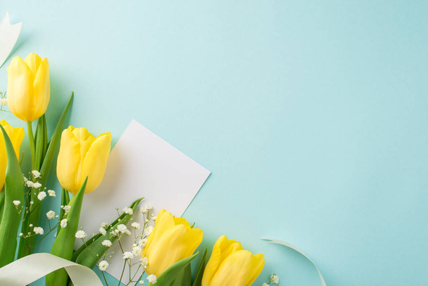 Top view photo of woman's day composition paper card bouquet of yellow tulips white gypsophila and white ribbon on isolated pastel blue background with blank space - Foto, immagini