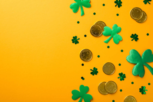 Top view photo of st patrick's day decorations green shamrocks clover shaped confetti and gold coins on isolated yellow background with copyspace - Foto, afbeelding