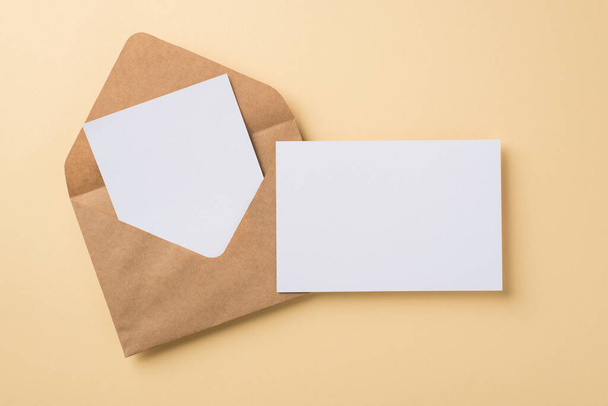 Κάτοψη του μεγάλου καφέ craft φάκελο με δύο λευκές κάρτες που βρίσκονται σε μπεζ απομονωμένο φόντο κενό χώρο - Φωτογραφία, εικόνα
