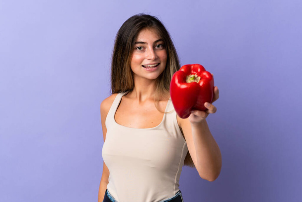 Young woman holding a pepper isolated on purple background with happy expression - Foto, Bild