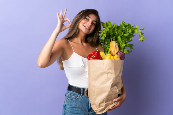 Młoda kobieta trzyma torbę na zakupy pokazuje znak ok palcami - Zdjęcie, obraz
