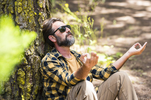 Homme barbu hipster adulte méditer et avoir une activité de loisirs de plein air de détente dans les bois de la forêt assis contre un tronc d'arbre et profiter de la nature sentiment et l'amour autour. Les hommes aiment la vie - Photo, image