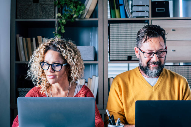 Взрослые мужчины и женщины работают вместе, улыбаясь на ноутбуке. Концепция современного семейного образа жизни и умных рабочих или цифровых профессий. Рабочее место в офисе - Фото, изображение
