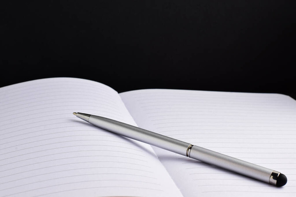 Silver ballpoint pen on notebook, black background. - Fotografie, Obrázek