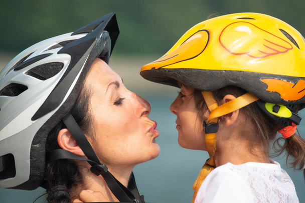 Retrato de una mujer sonriente con su hija lista para montar en bicicleta y usar cascos, enviándose besos - Foto, imagen